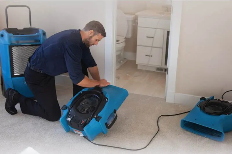 A technician setting a blue air mover to dry a room